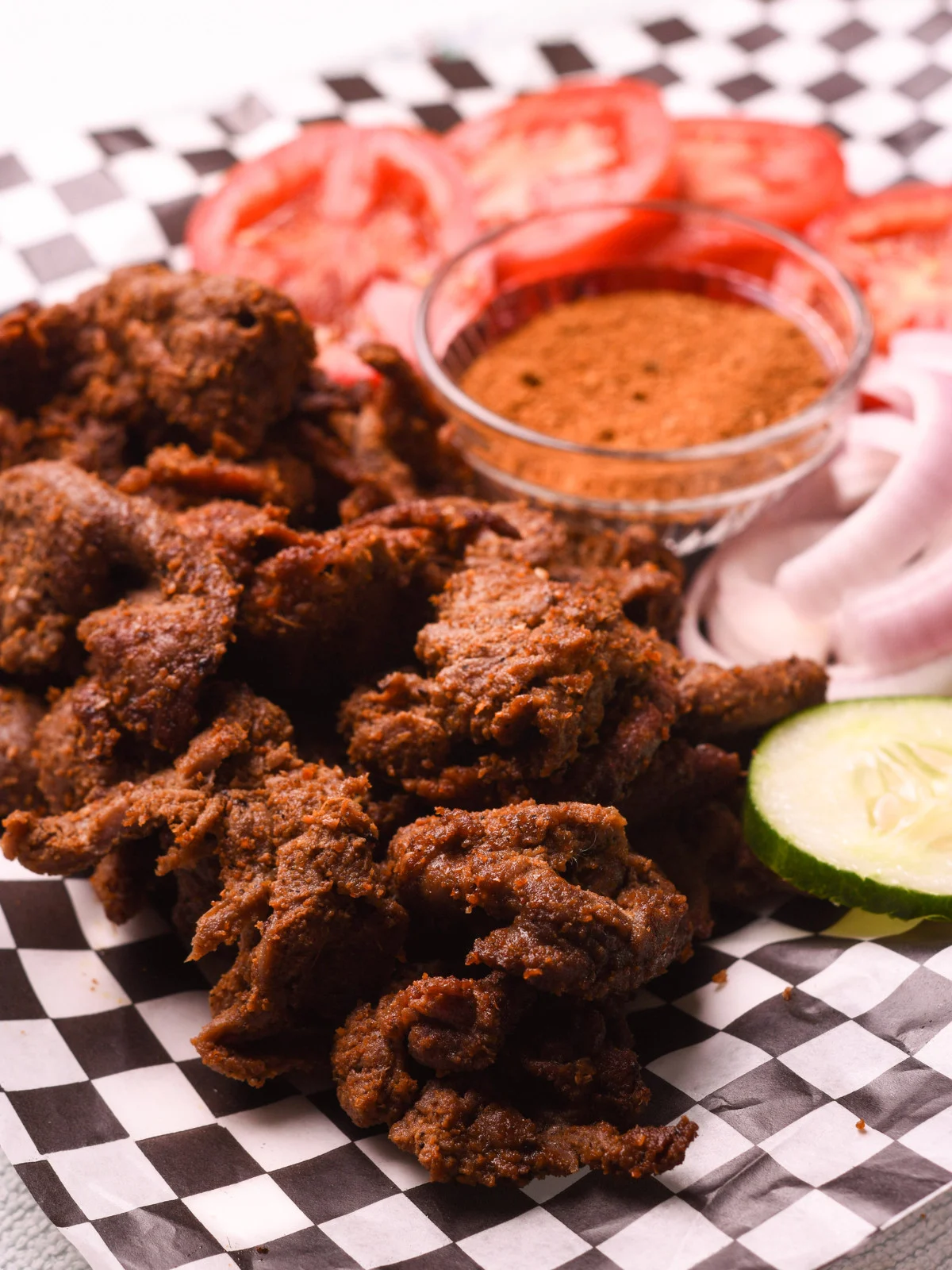 Smoky Naija-style suya — charcoal-grilled spiced beef with red onions, tomato and cucumber on checkered paper